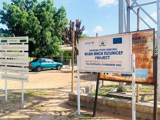 Signs for a UNICEF project in a rural area, with a blue car and trees in the background, promoting health initiatives.