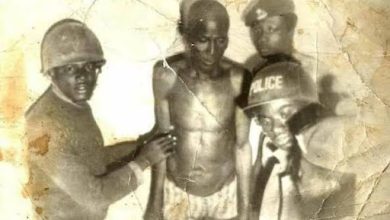 A group of men in uniform, some wearing helmets, surround a shirtless man in an old, worn photograph.