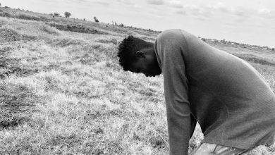 A person stands bent over on a grassy field under a cloudy sky in monochrome.