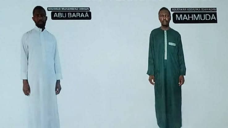 Two men in traditional clothing stand against a white background, one in a white robe labeled "Abu Baraa" and the other in green labeled "Mahmuda."