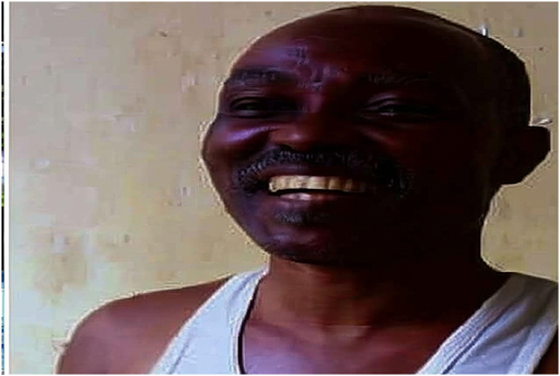 Smiling man in a white tank top stands against a light-colored wall.