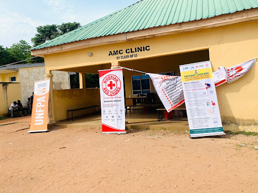 Exterior of AMC Clinic with banners from UNFPA, Red Cross, and UNICEF promoting health initiatives, under a bright sky.