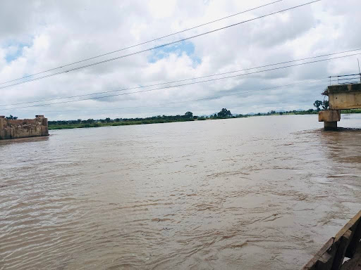 Wide river view with cloudy sky and distant greenery, featuring parts of an old and modern bridge on the sides.