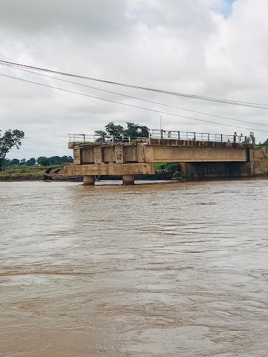 A concrete bridge spans a wide, calm river under a cloudy sky.