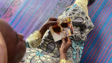 Person in patterned clothing sits on a mat, holding a small photo with two people in it, faces blurred.