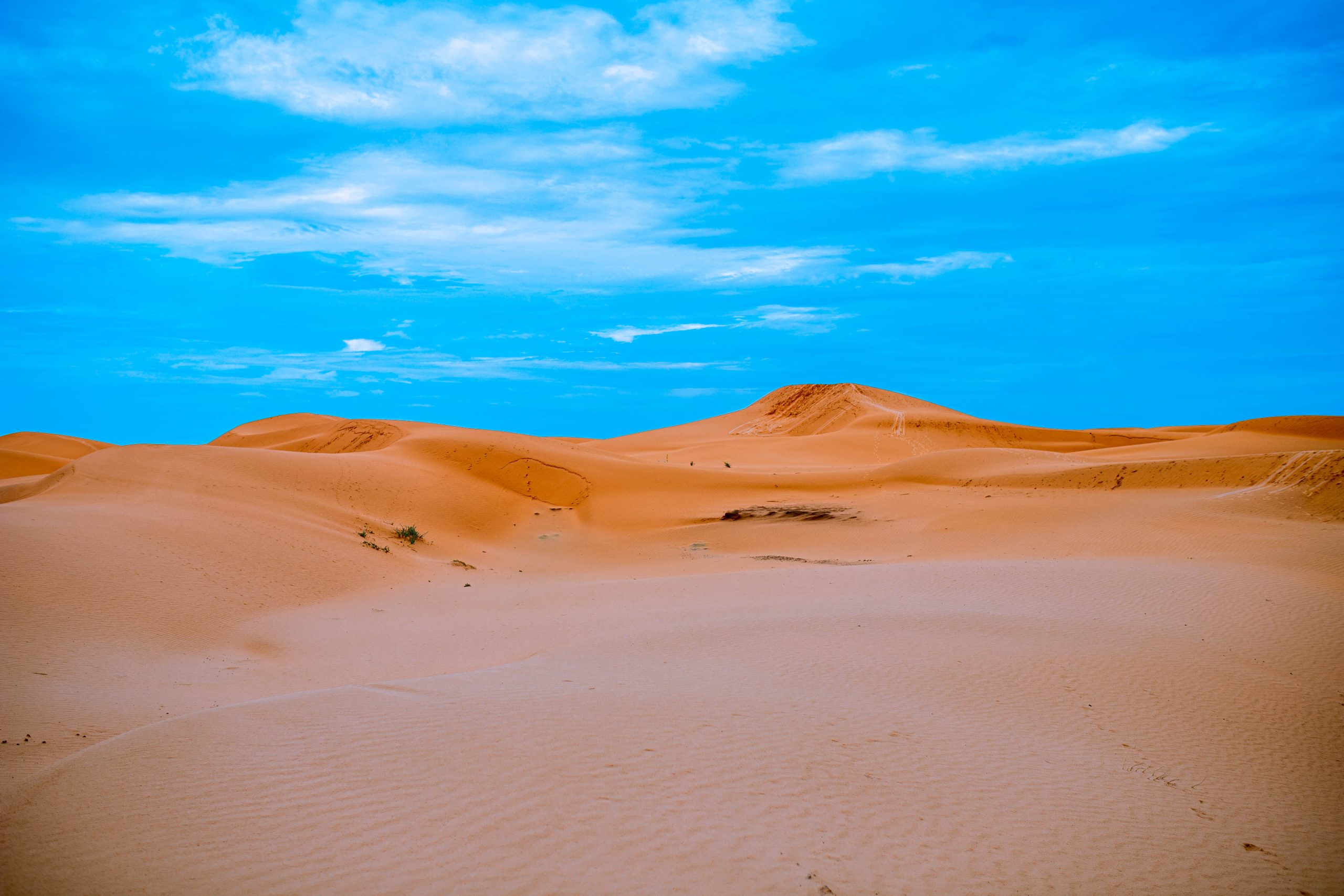 Vast orange sand dunes under a bright blue sky with wispy clouds.