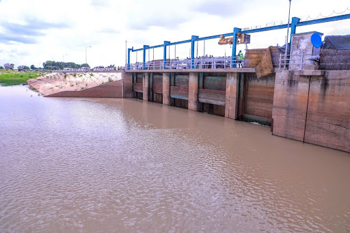 Water flowing through a concrete dam with a blue and gray structure on a cloudy day.