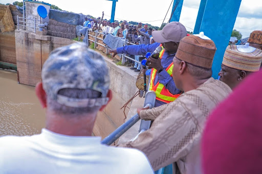 Group of people gathered at a water control structure, with one person pointing towards the water.