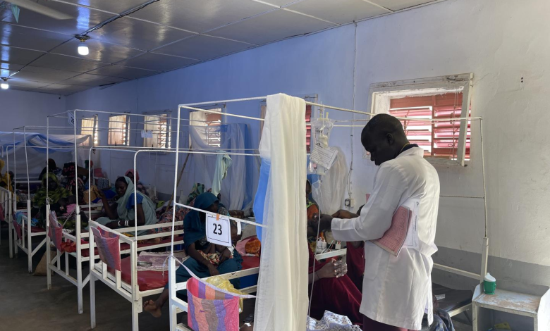 Doctor attending to a patient in a hospital ward with several beds and numbered partitions.