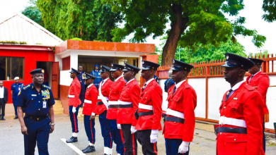 fire service in Nigeria Uniformed officers in red stand in formation, while a commanding officer in navy blue inspects them, with trees and buildings in the background.