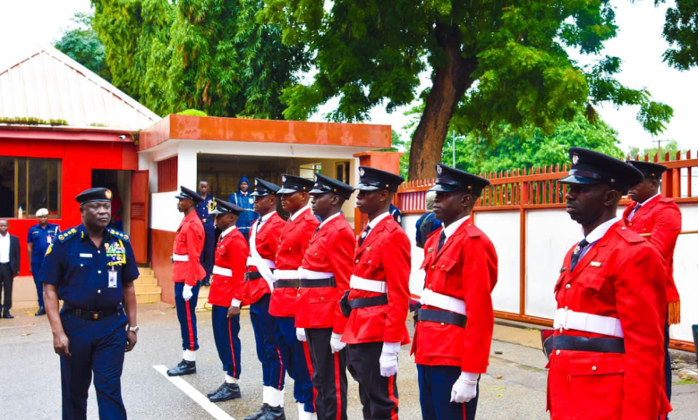 fire service in Nigeria Uniformed officers in red stand in formation, while a commanding officer in navy blue inspects them, with trees and buildings in the background.
