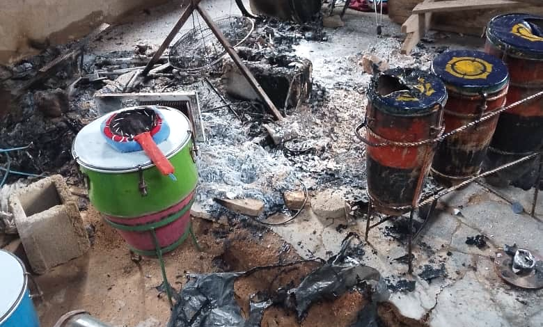 A cluttered room with drums, debris, and burnt remains of equipment scattered on the floor.