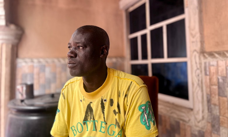 Man in a yellow T-shirt sits indoors, looking to the side.