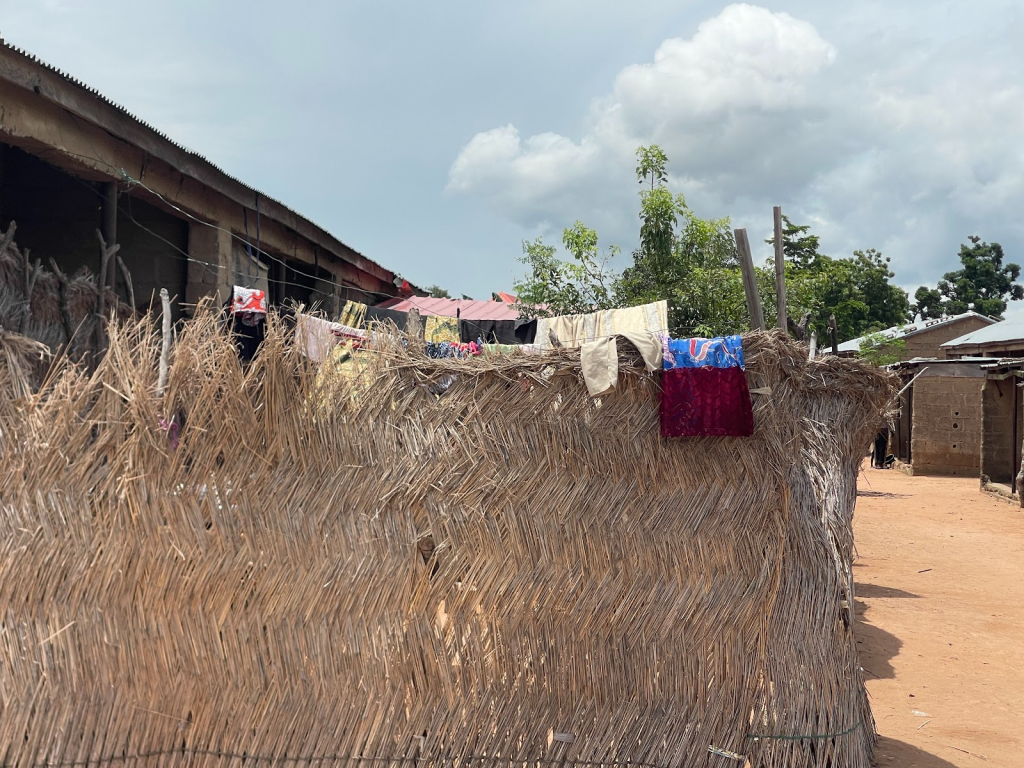 Woven straw fence with colorful clothes drying on top, sunny day with clouds in the background.