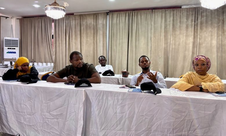 Five people seated at a conference table in a room with chandeliers and curtains.