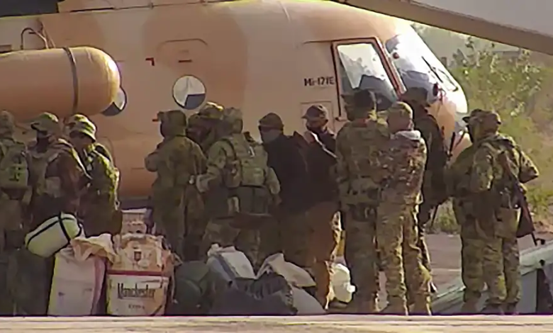 Soldiers in camouflage gear stand near a brown helicopter, with bags and supplies on the ground.