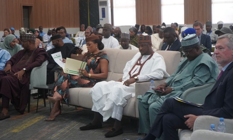 People seated in a conference room, engaged in reading and discussions, with documents and water bottles on tables in front of them.