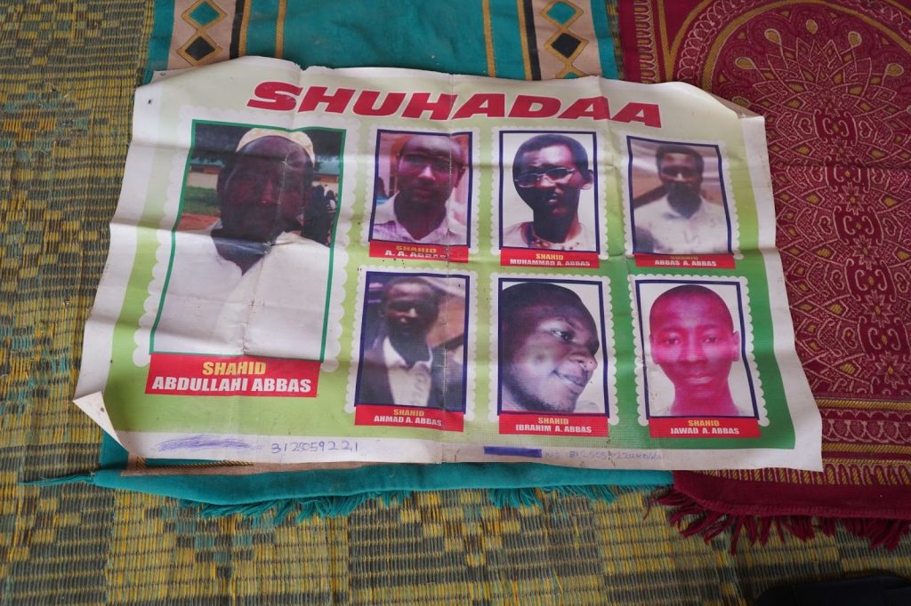 A poster with eight portraits titled "Shuhadaa," laying on patterned fabric.