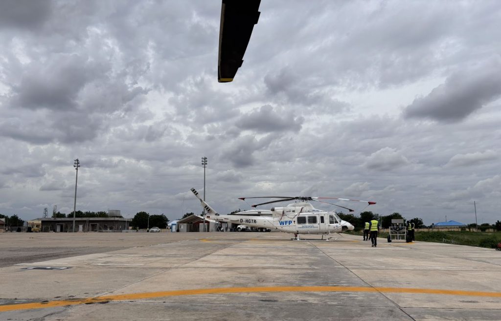 Helicopter on a cloudy runway with crew members in high-visibility vests nearby, preparing equipment.