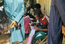 People registering at an outdoor table, with one person writing on forms and others standing nearby, holding phones.