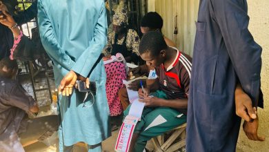People registering at an outdoor table, with one person writing on forms and others standing nearby, holding phones.