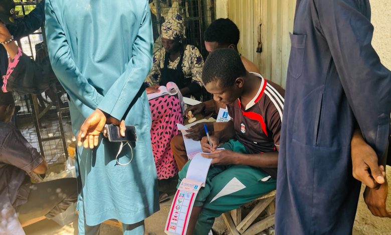 People registering at an outdoor table, with one person writing on forms and others standing nearby, holding phones.