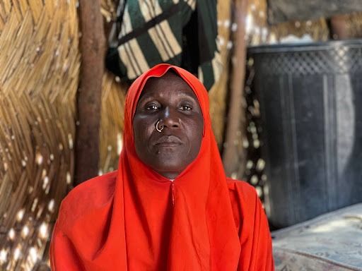 A person in a bright red headscarf sits indoors, with woven material in the background.
