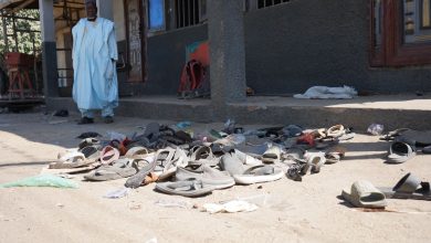 Sandals scattered on the ground outside a building with a person standing near the entrance.