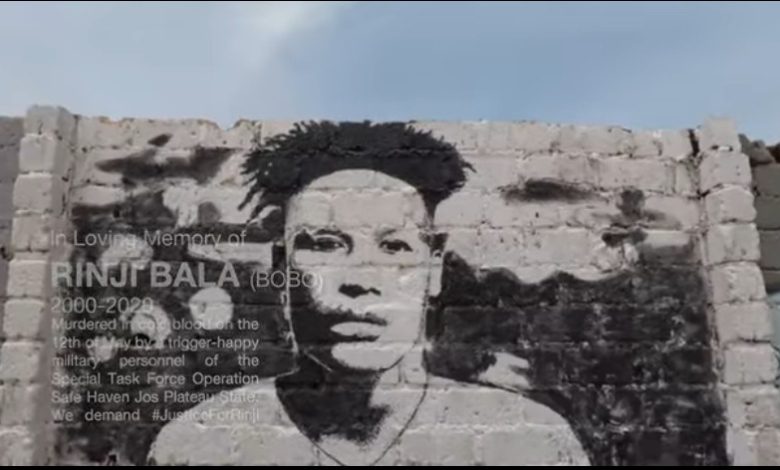 Mural on a brick wall depicting a person's face with a memorial text remembering Rinji Bala and calling for justice.