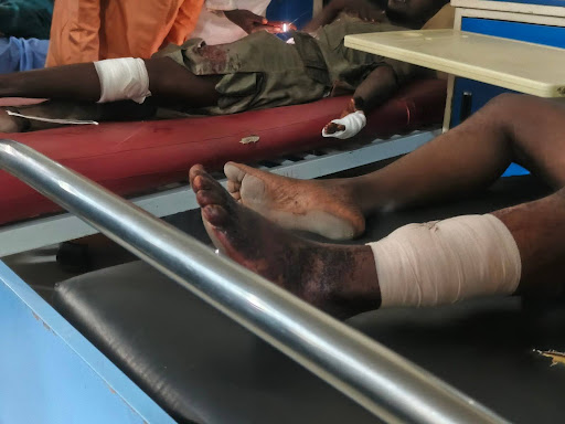 Two individuals with bandaged limbs lying on hospital beds, receiving medical care.