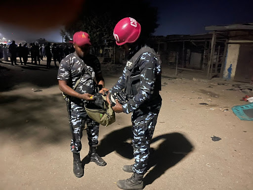 Two uniformed individuals in helmets exchanging items on a dimly lit street at night.