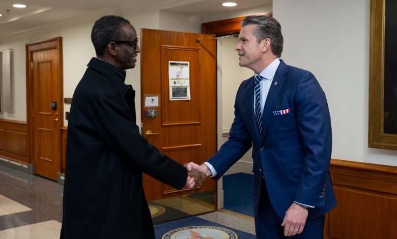 Two men in formal attire shaking hands in a hallway with wood paneling.