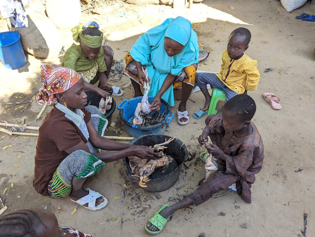 A group of people, including children, cleaning chickens outdoors.