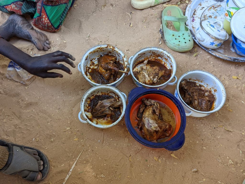 Cooked meat in five bowls on the ground beside a person's hand and foot, scattered plates, and a single green shoe.