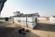 Simple structures with tarpaulin walls in a dusty, open area under a clear sky.