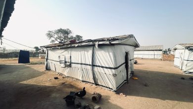 Simple structures with tarpaulin walls in a dusty, open area under a clear sky.