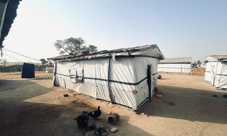 Simple structures with tarpaulin walls in a dusty, open area under a clear sky.