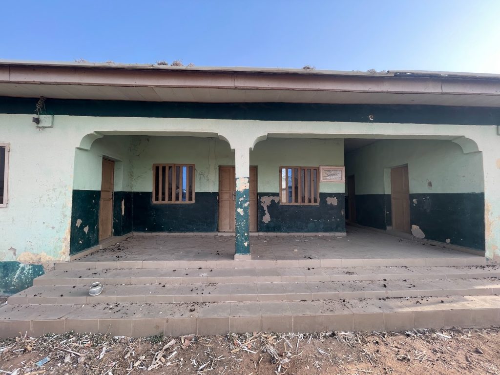 A weathered building with three doorways and peeling paint, viewed from the front, under a clear blue sky.