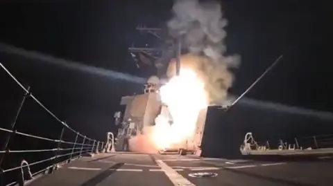Ship launching a missile at night with flames and smoke visible against the dark sky.