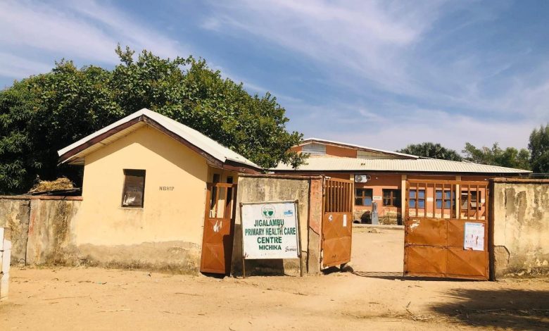 A rural health center with open gates, surrounded by trees under a blue sky.