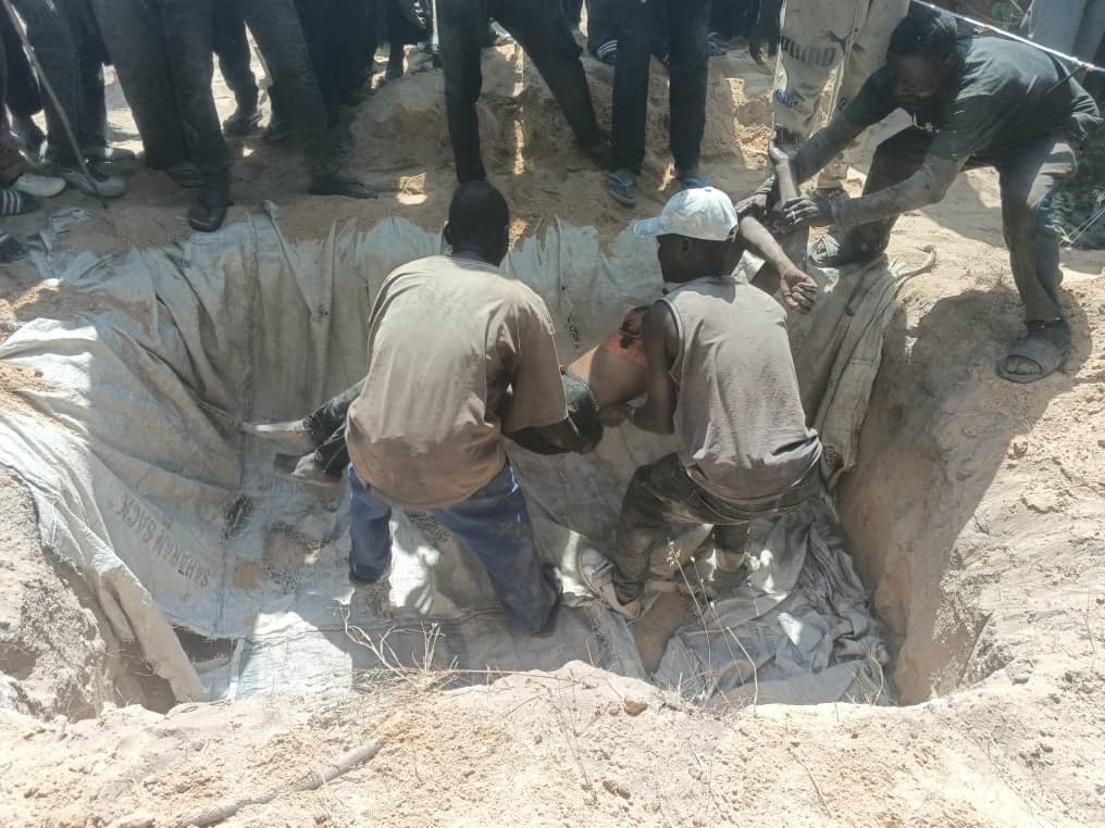 Group of people around a large pit, lifting a person out using a sheet.