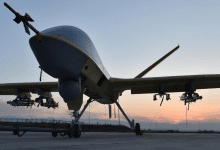 Drone with mounted equipment on a runway, silhouetted against a sunset sky.