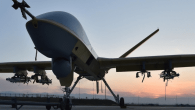 Drone with mounted equipment on a runway, silhouetted against a sunset sky.