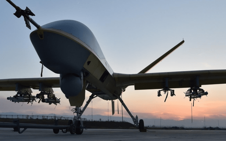 Drone with mounted equipment on a runway, silhouetted against a sunset sky.