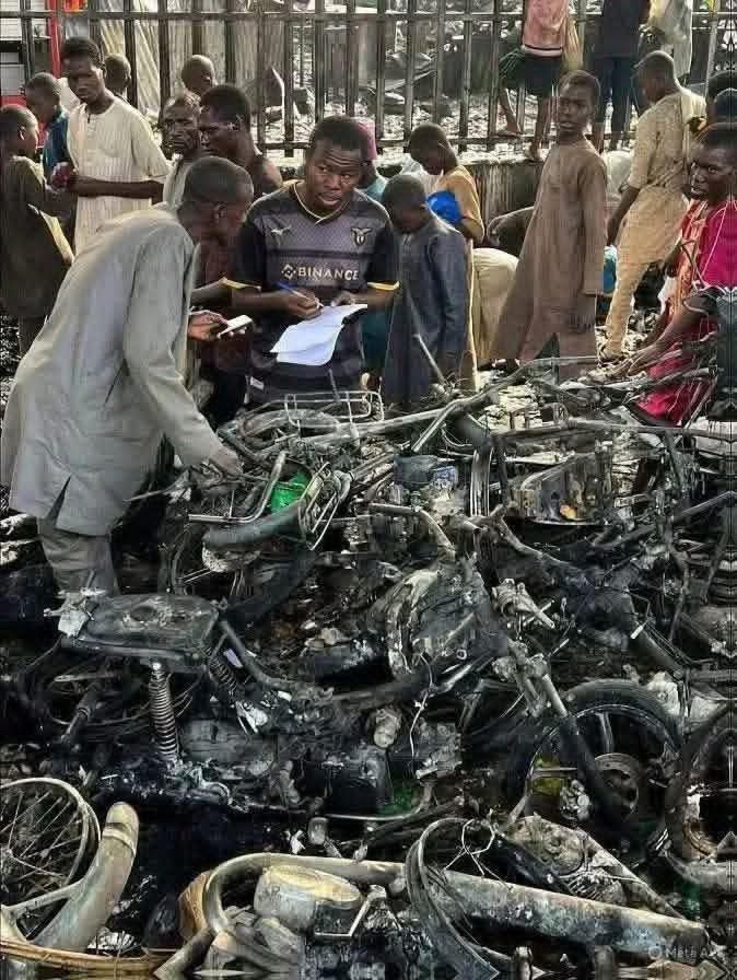 People examine the charred remains of motorcycles amidst a crowd.