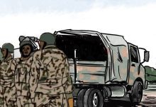 Soldiers in camouflage stand near a military truck with a covered cargo area under a blue sky.