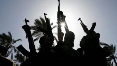 Silhouettes of people holding rifles against a bright sky with palm trees in the background.