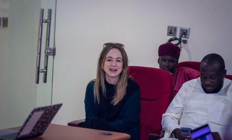 Three people seated, one woman smiling, two men beside her, one using a phone. A laptop is open on the table.