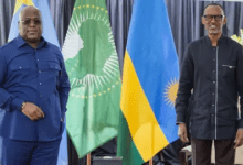 Two men stand in front of African Union and national flags, engaged in a formal setting.