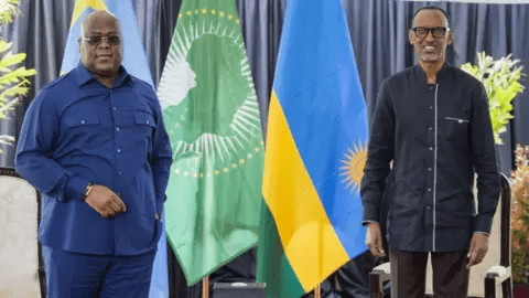 Two men stand in front of African Union and national flags, engaged in a formal setting.